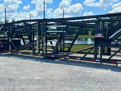 Rows of stacked rectangular and square American-sourced steel tubes and beams stretch into the background of a manufacturing facility, with a person visible in the distance.