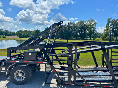Rows of stacked rectangular and square American-sourced steel tubes and beams stretch into the background of a manufacturing facility, with a person visible in the distance.