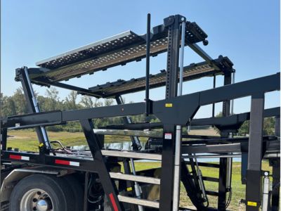 Rows of stacked rectangular and square American-sourced steel tubes and beams stretch into the background of a manufacturing facility, with a person visible in the distance.